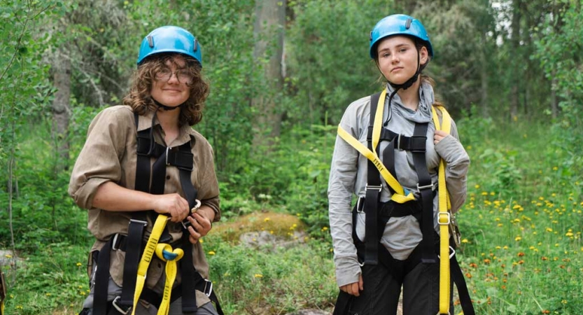 Two students wearing rock climbing safety gear pose for a photo amid thick greenery